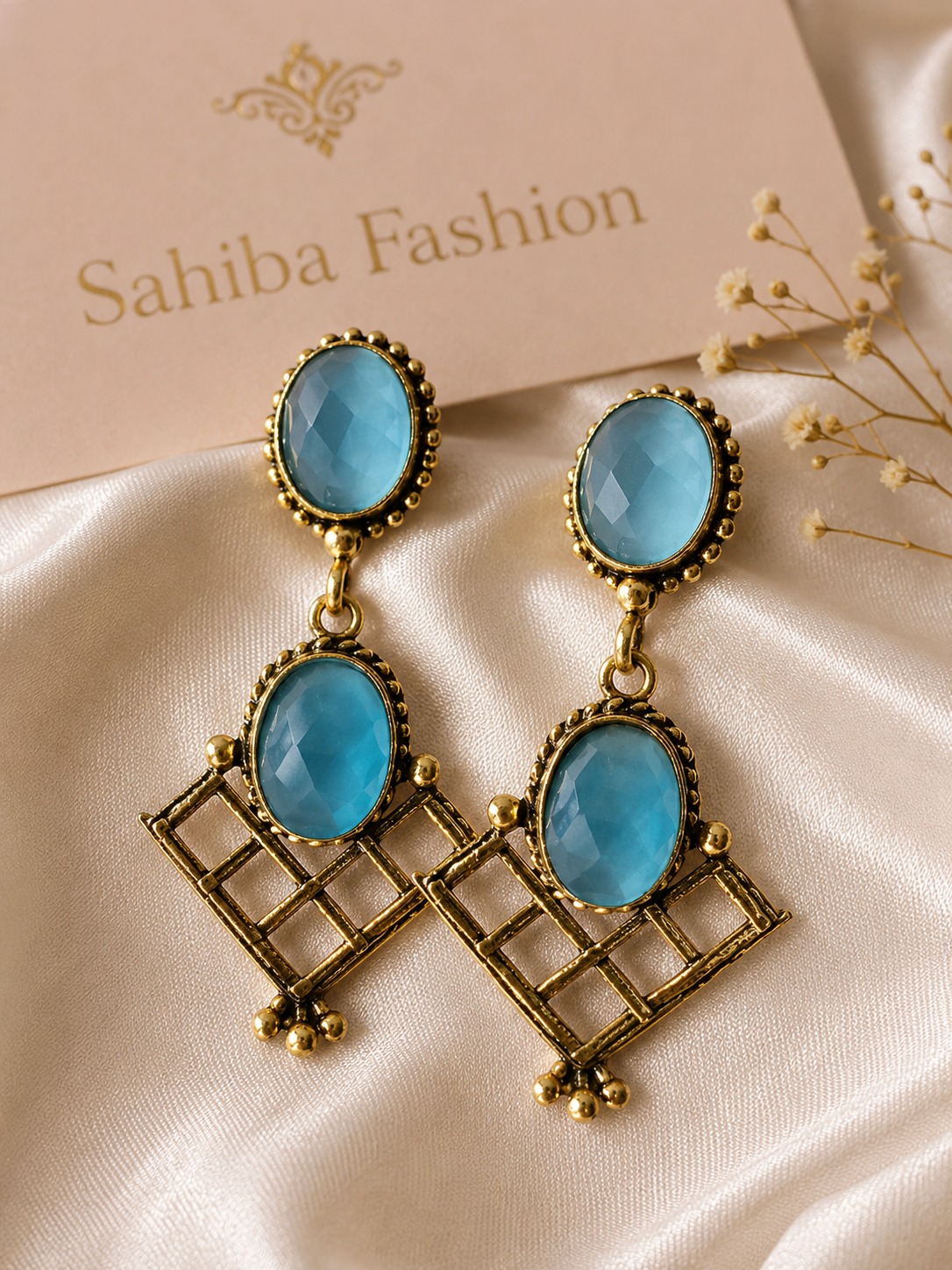 red pearl chandbali earrings with beads | anti tarnish festive statement jhumka Pair of vintage-style antique gold drop earrings featuring oval sky blue stones and geometric grid patterns on a satin cloth background.