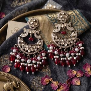 Luxury display of a pair of large silver crescent earrings with kundan work, pearls, and red hanging beads on dark grey velvet cloth.