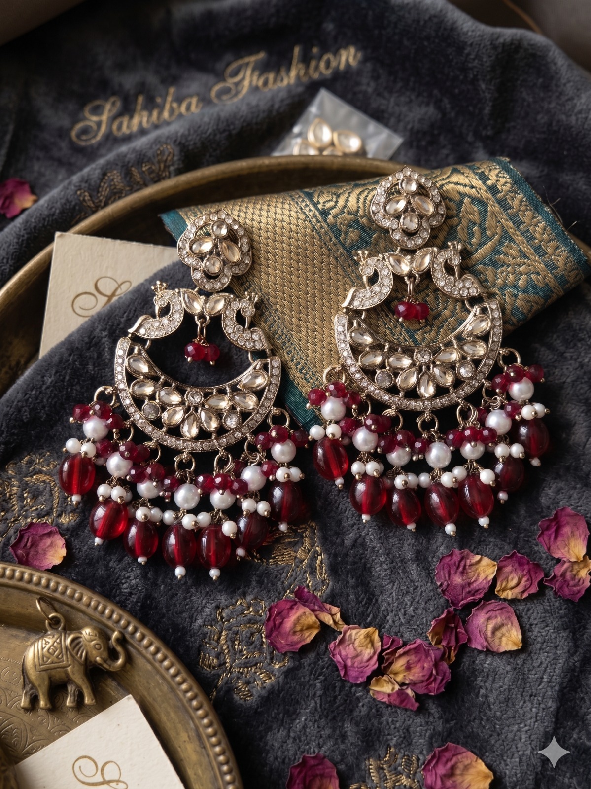 red pearl chandbali earrings with beads | anti tarnish festive statement jhumka Luxury display of a pair of large silver crescent earrings with kundan work, pearls, and red hanging beads on dark grey velvet cloth.