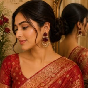 Woman wearing traditional maroon stone earrings with pearl beads and red Banarasi silk saree
