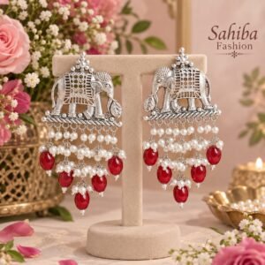 Sahiba Fashion silver elephant motif earrings with white pearl and red bead drops on a metal display stand in a floral setting.