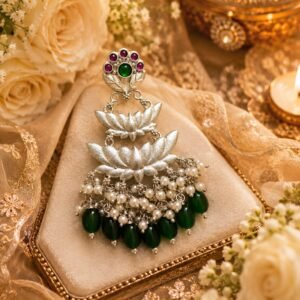 Flat-lay product shot of a silver lotus statement earring with green beads and pearl tassels on a neutral surface.